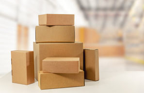 several sizes of cardboard boxes on a white surface in a blurred warehouse setting.